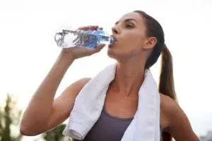 Woman drinking water after workout outdoors.