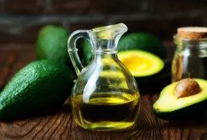 Avocado oil in glass pitcher with fresh avocados.