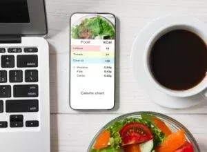 Smartphone displaying calorie chart beside salad and coffee.