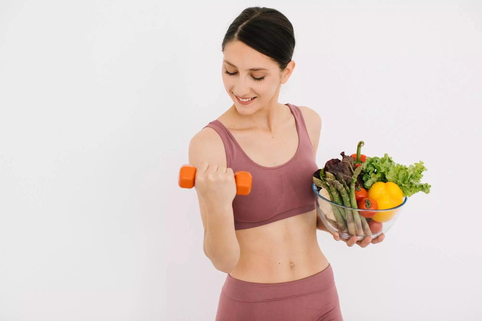 Woman exercising with dumbbell and holding healthy food.