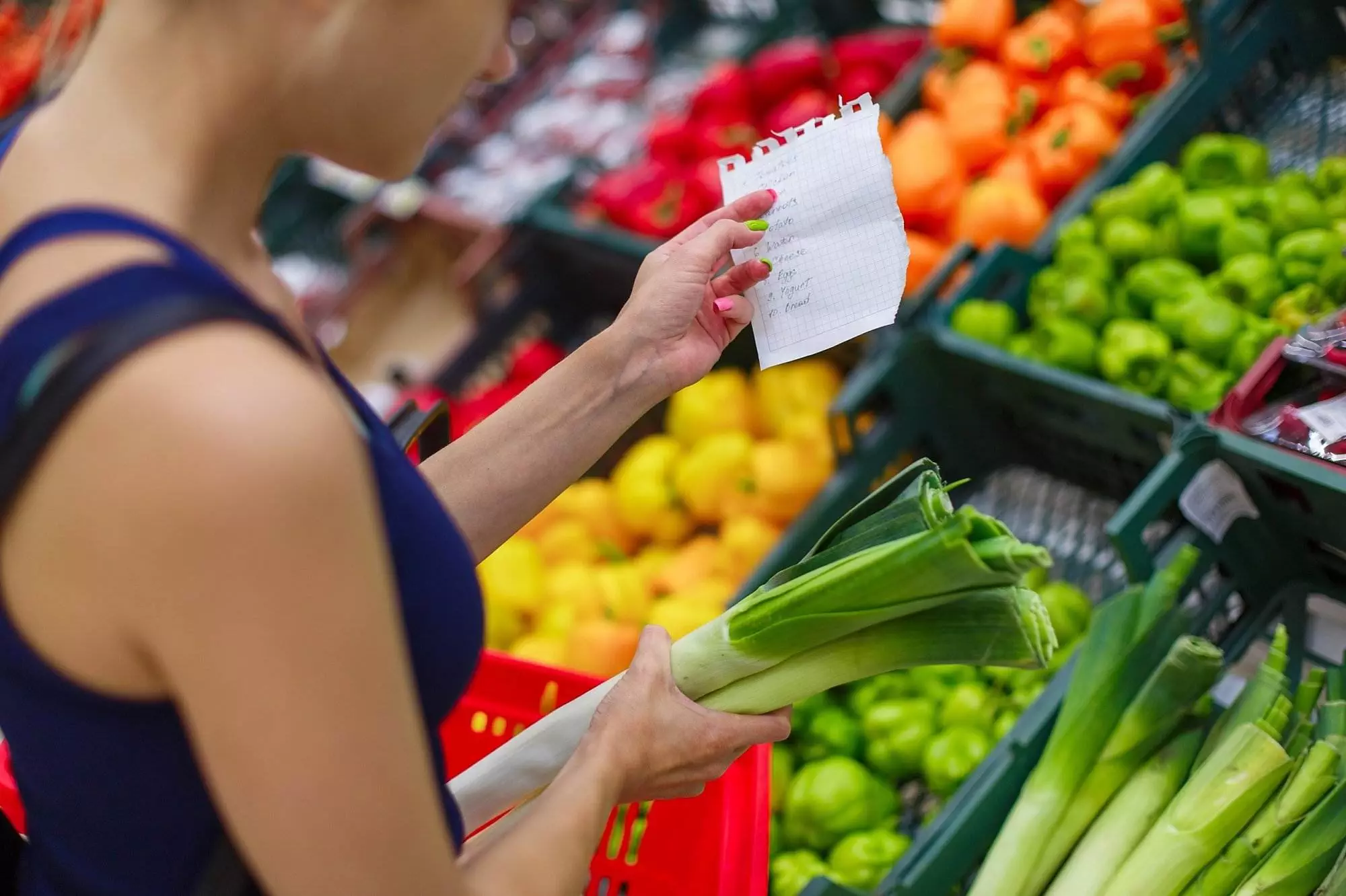 Woman checking shopping list in grocery store produce aisle.