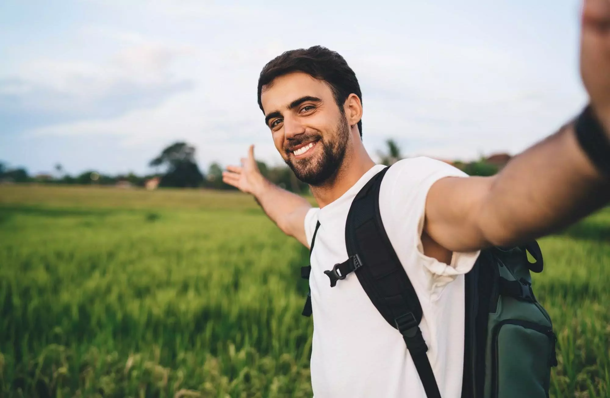 Man taking selfie in green field with backpack.