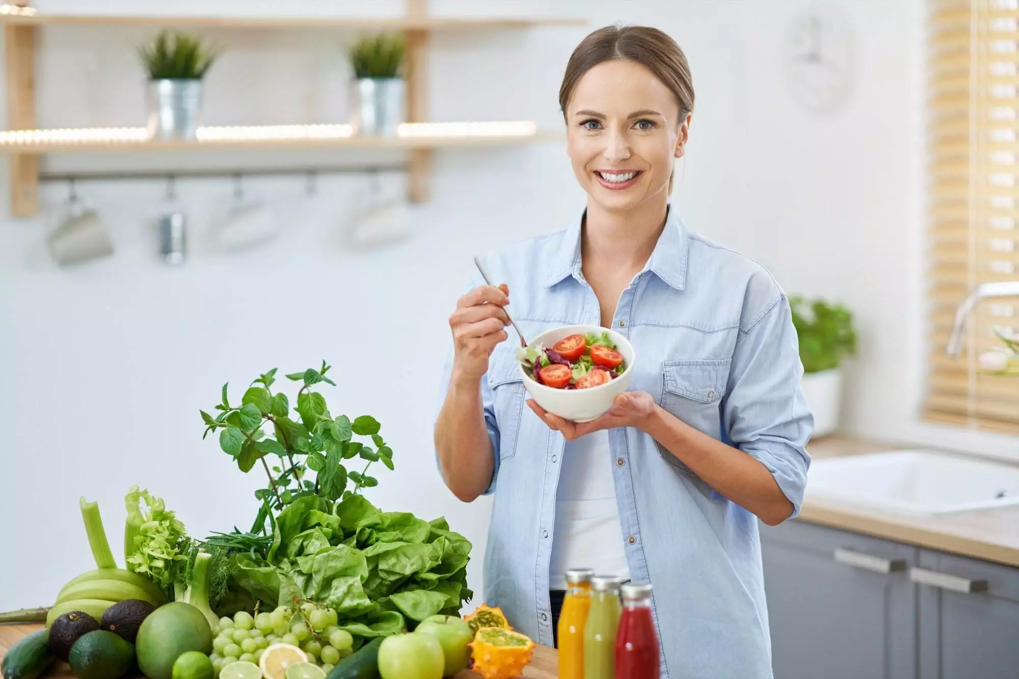 Woman holding fresh vegetable salad in kitchen.