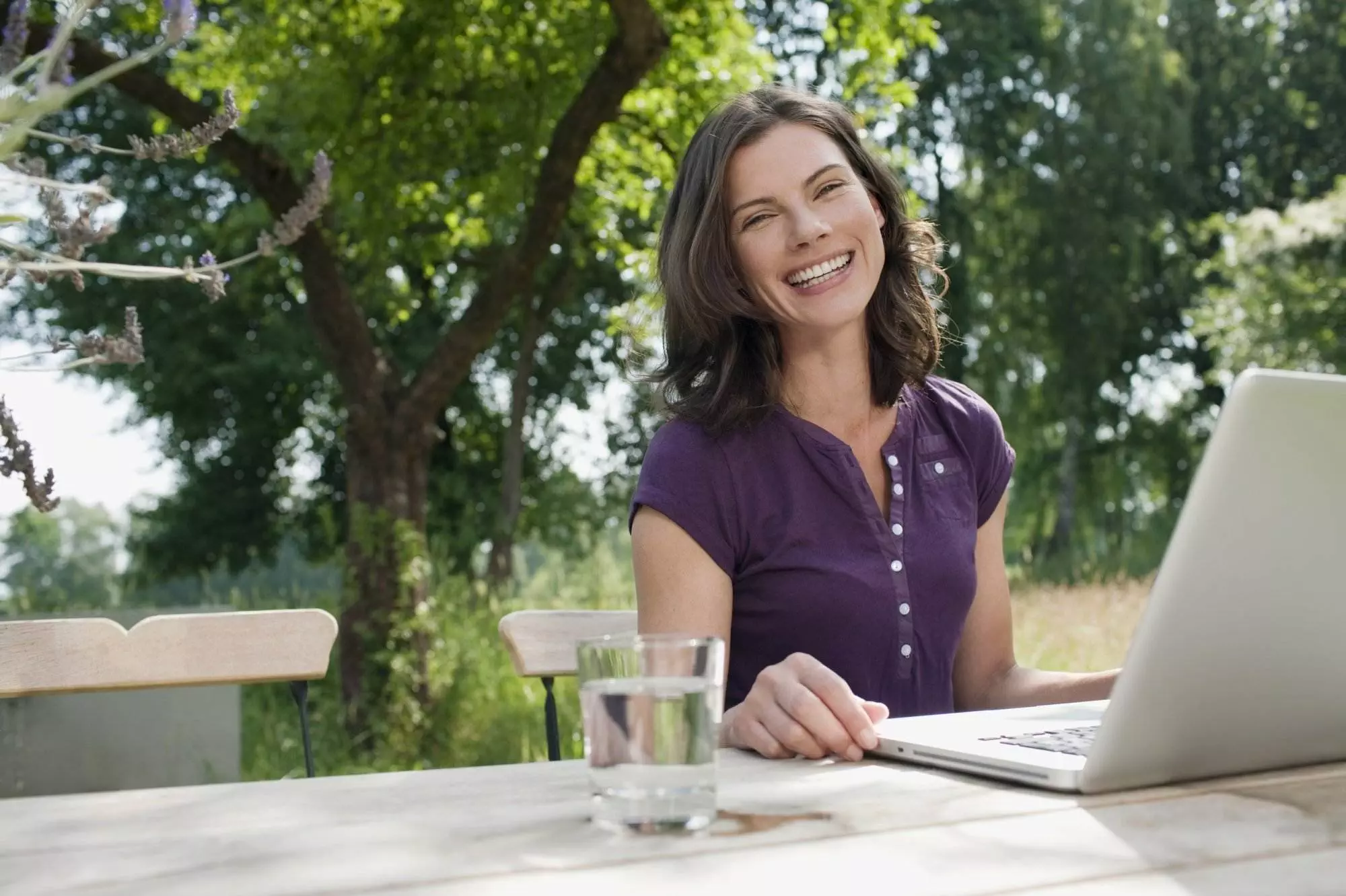 Woman working on laptop outdoors smiling.