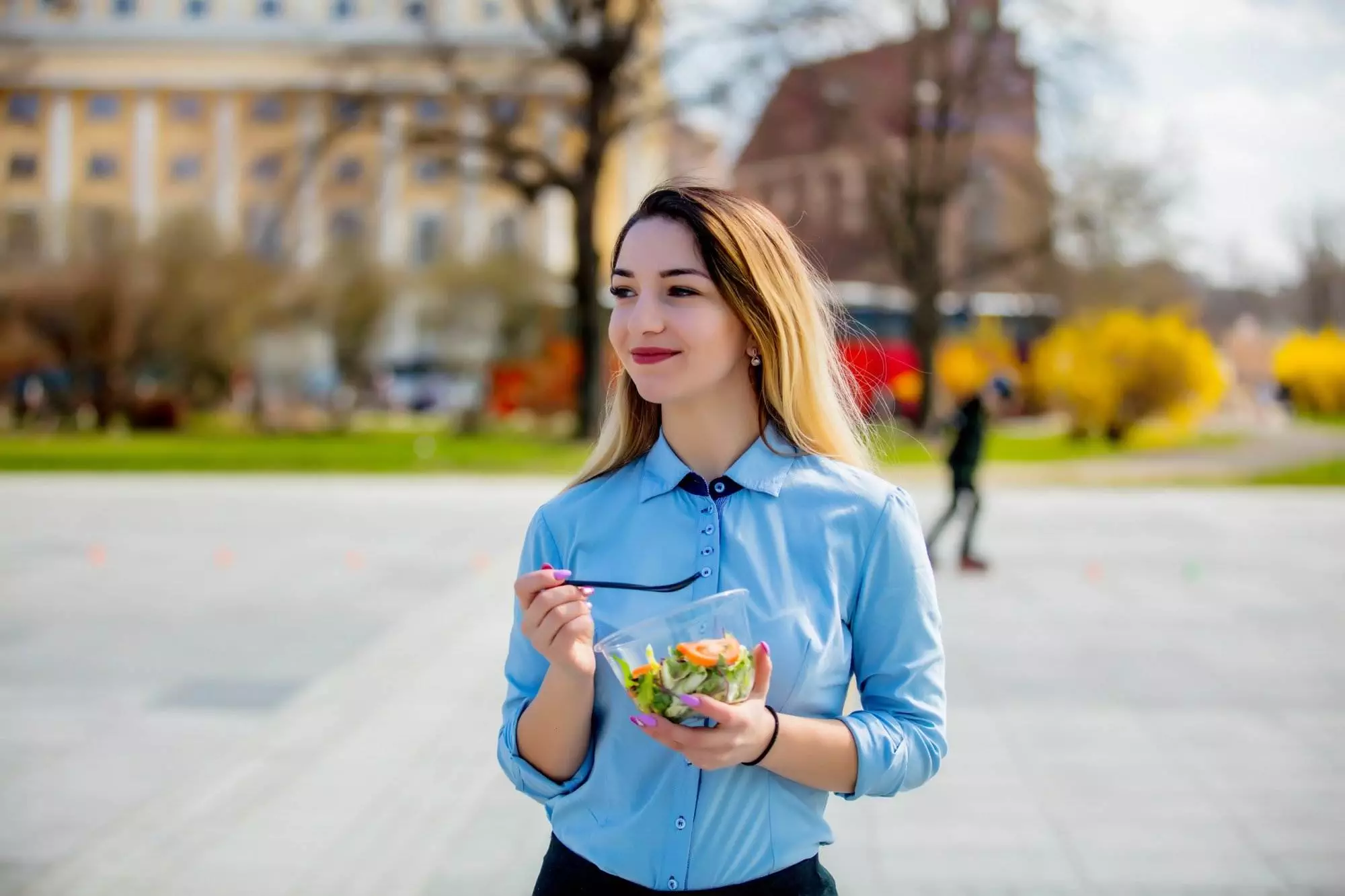 Woman eating salad outdoors on sunny day