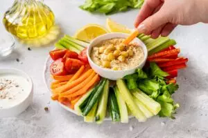 Hand dipping carrot into hummus with fresh veggies.