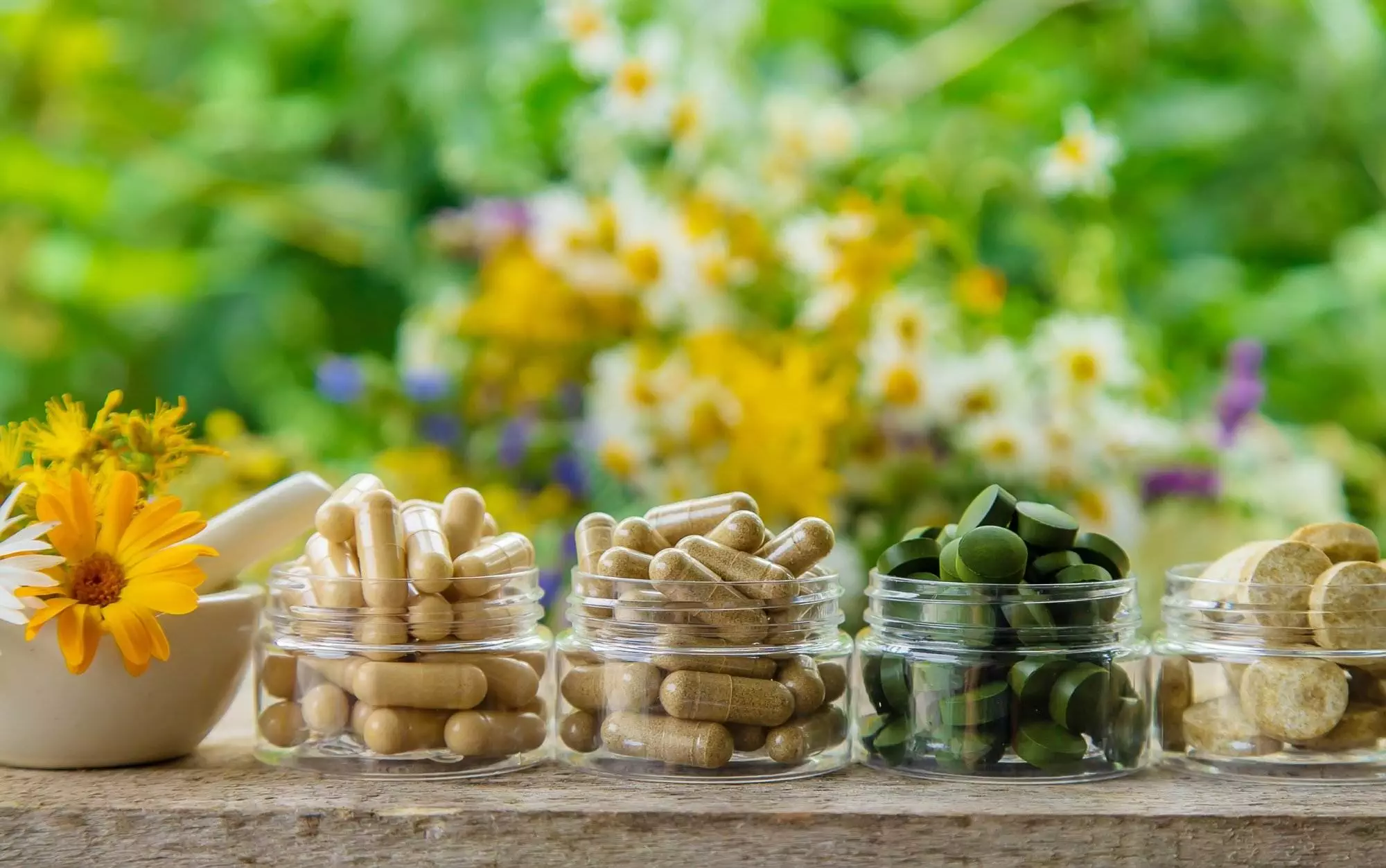 Herbal supplements and flowers on wooden table.