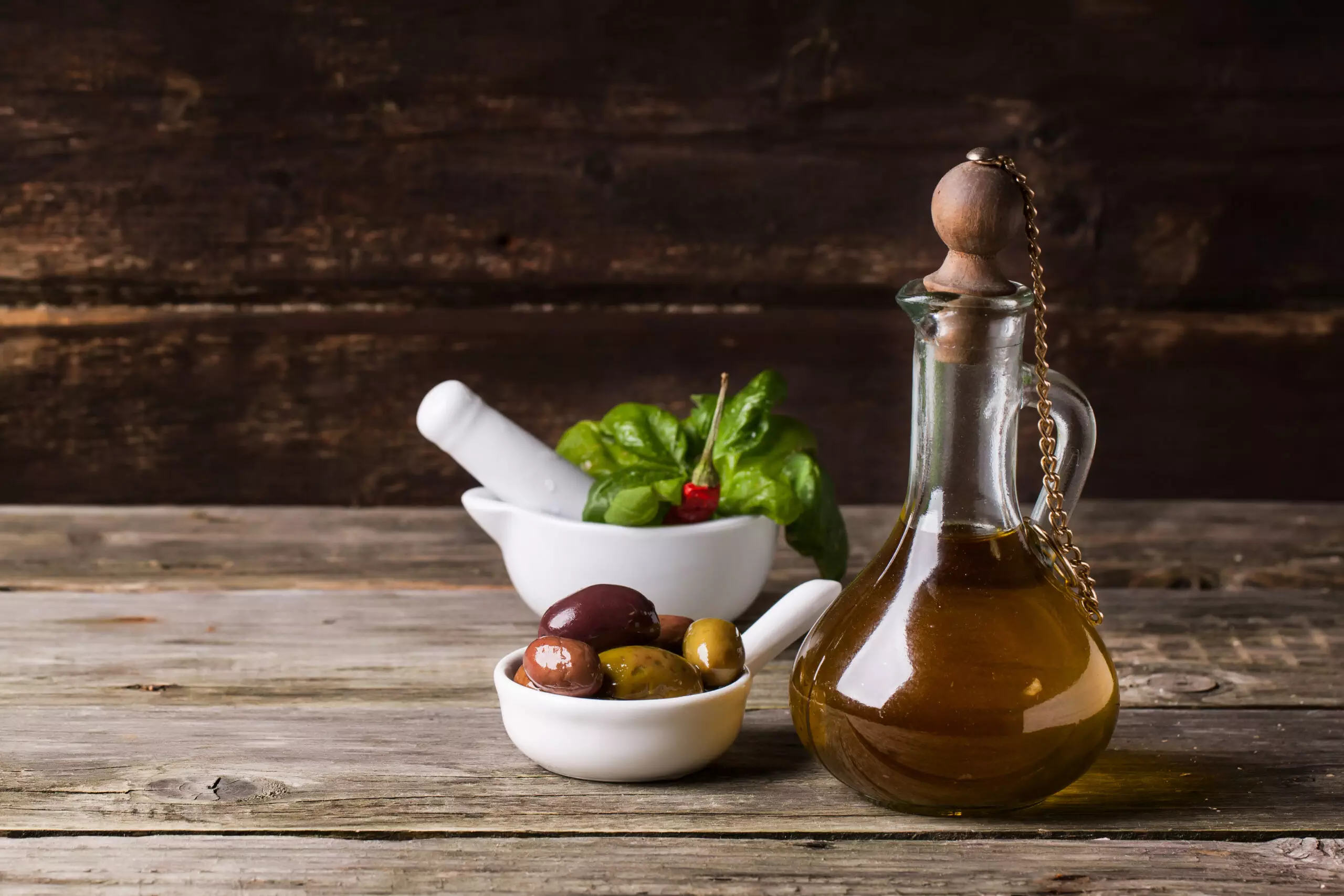 Olive oil, olives, pestle, and basil on wood.