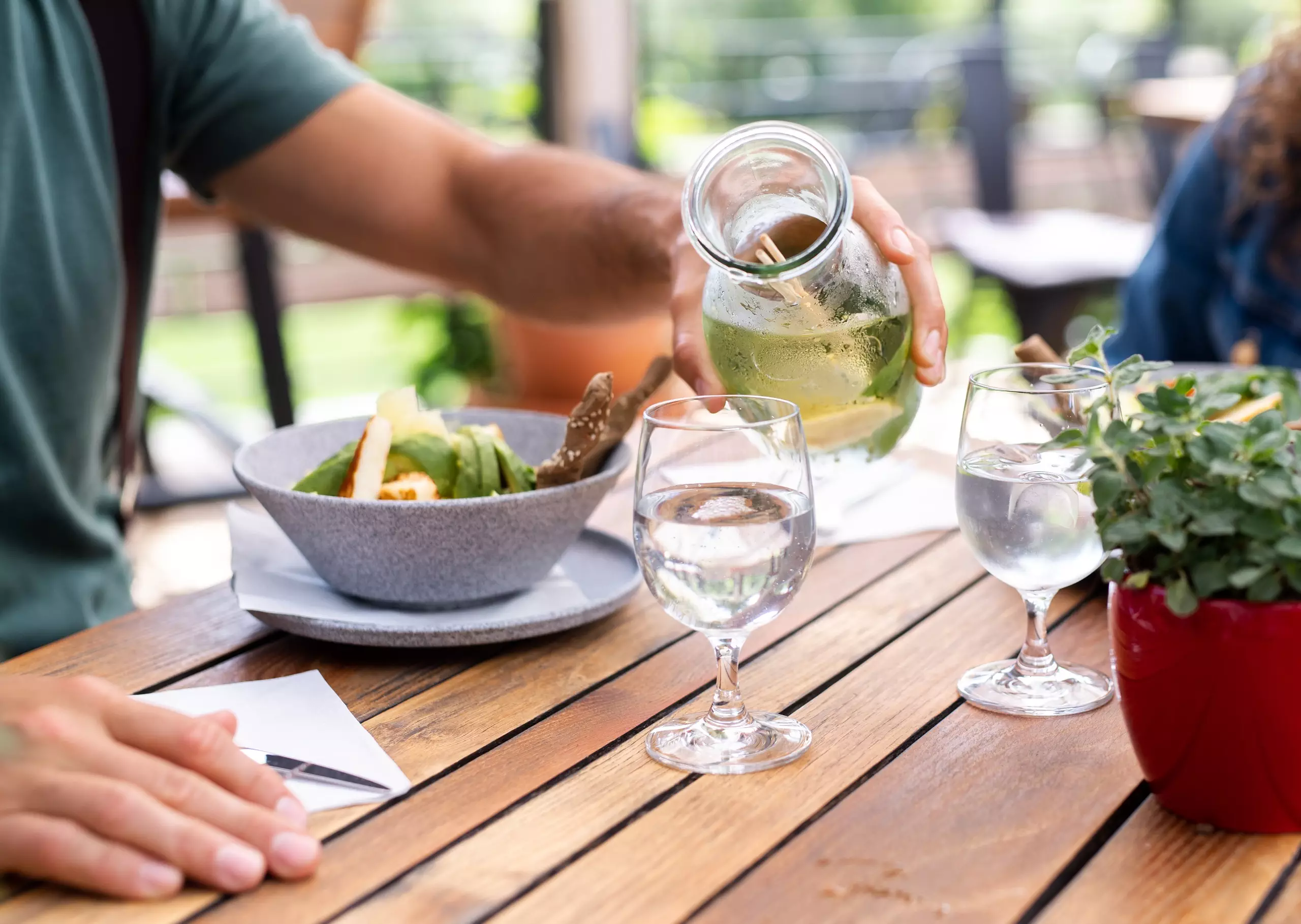 Pouring water at outdoor dining table with food.