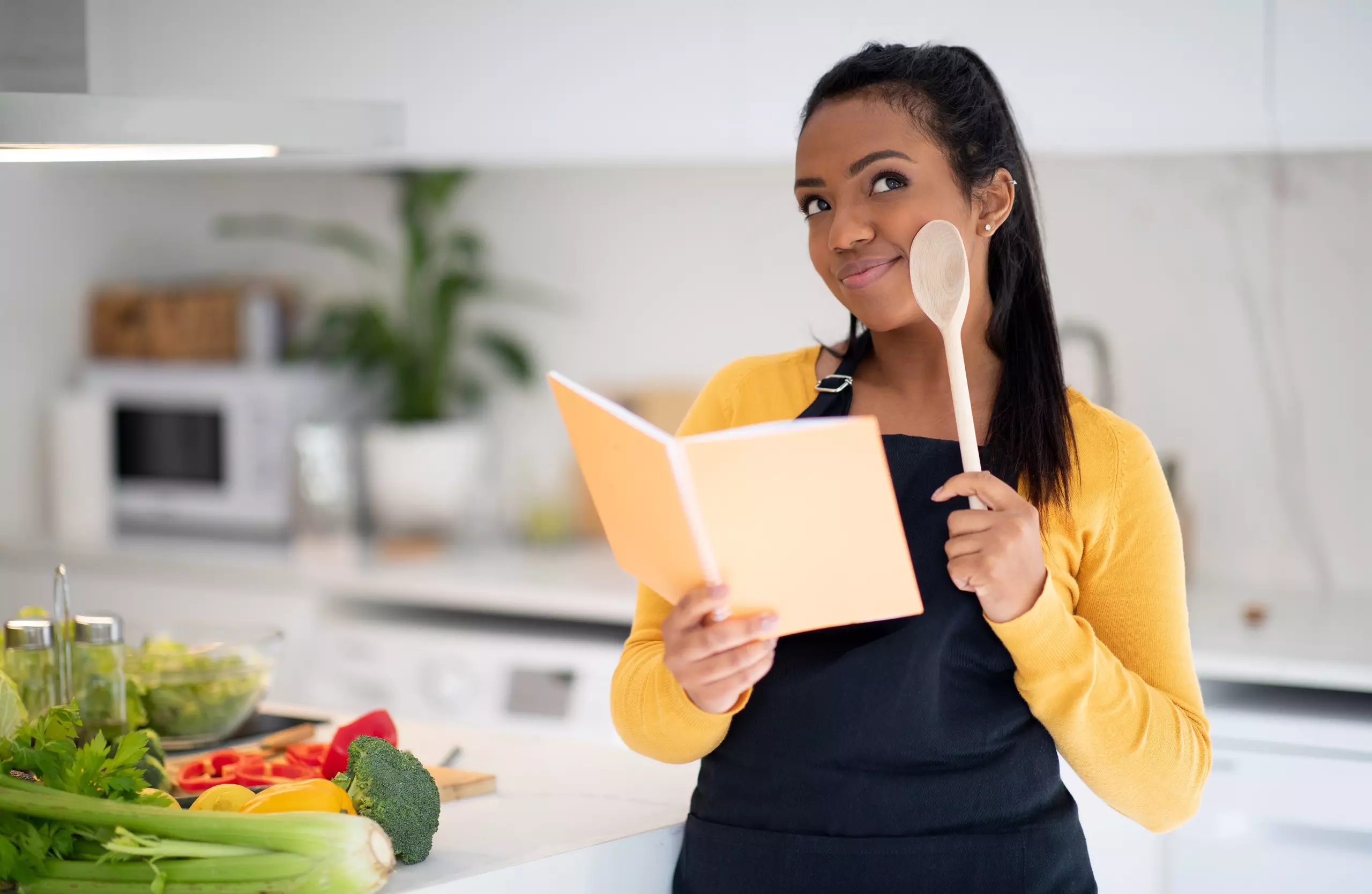 Woman reading recipe in kitchen with fresh vegetables.