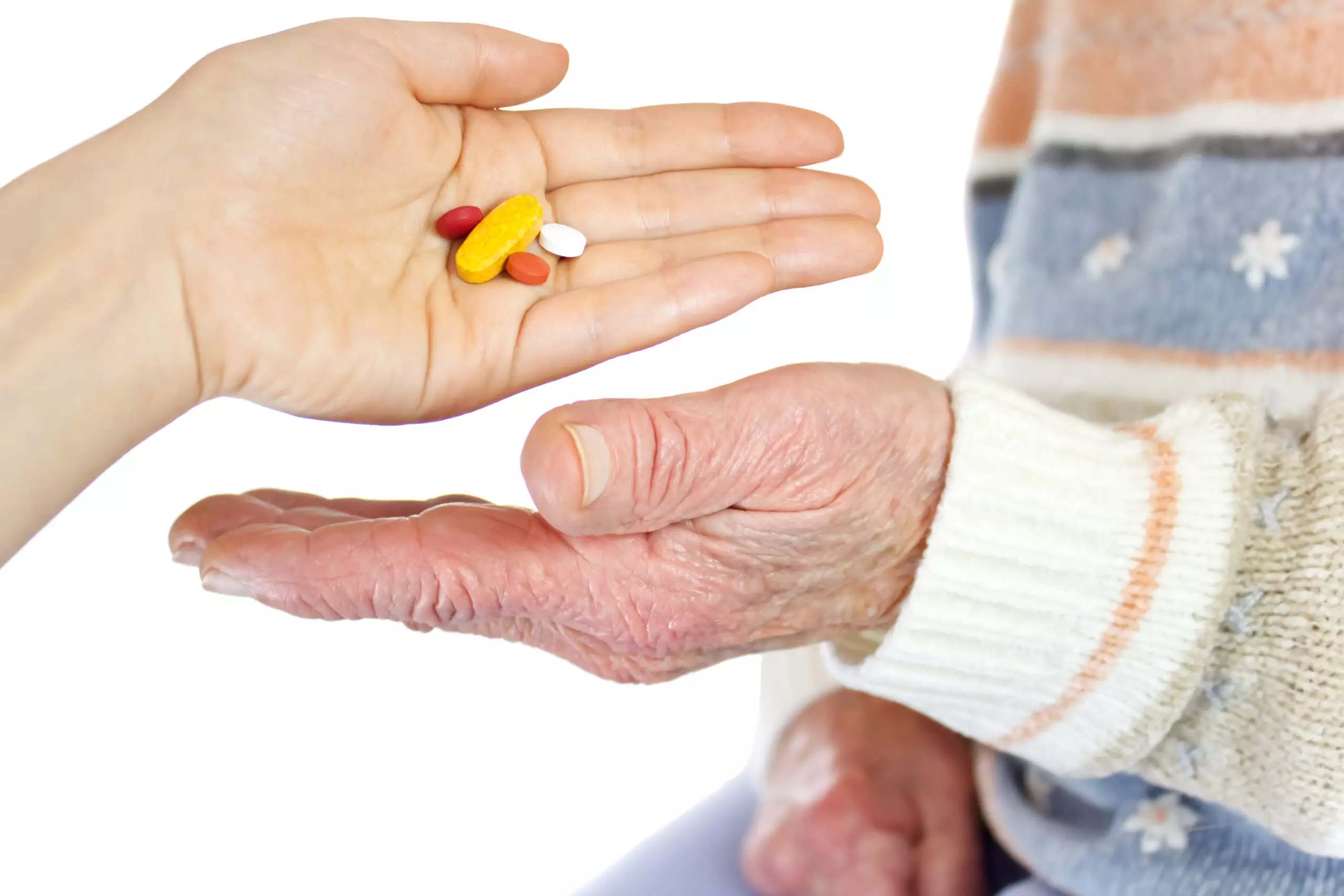 Hand giving medication to elderly person.