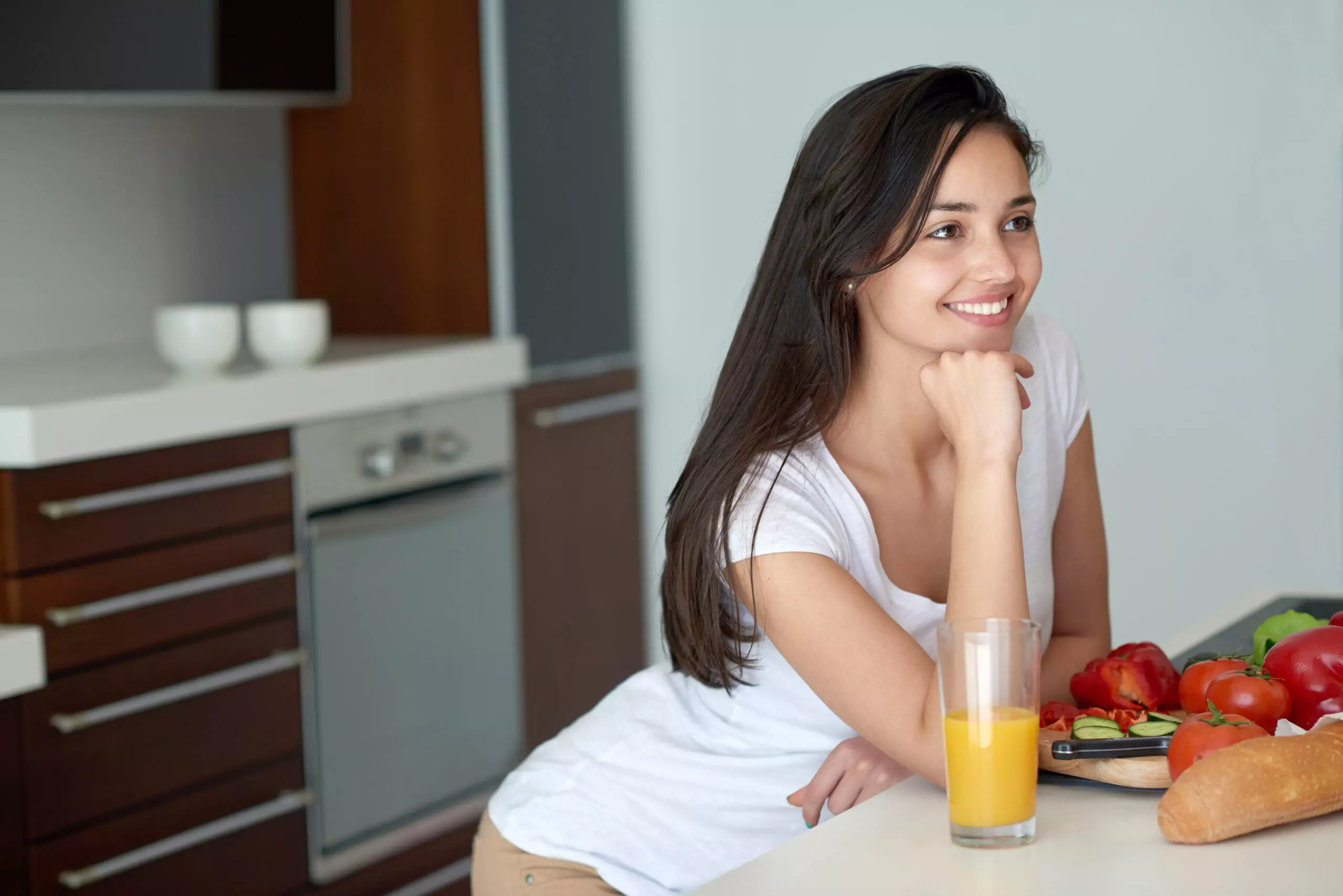 Woman smiling in kitchen with fresh vegetables and juice.