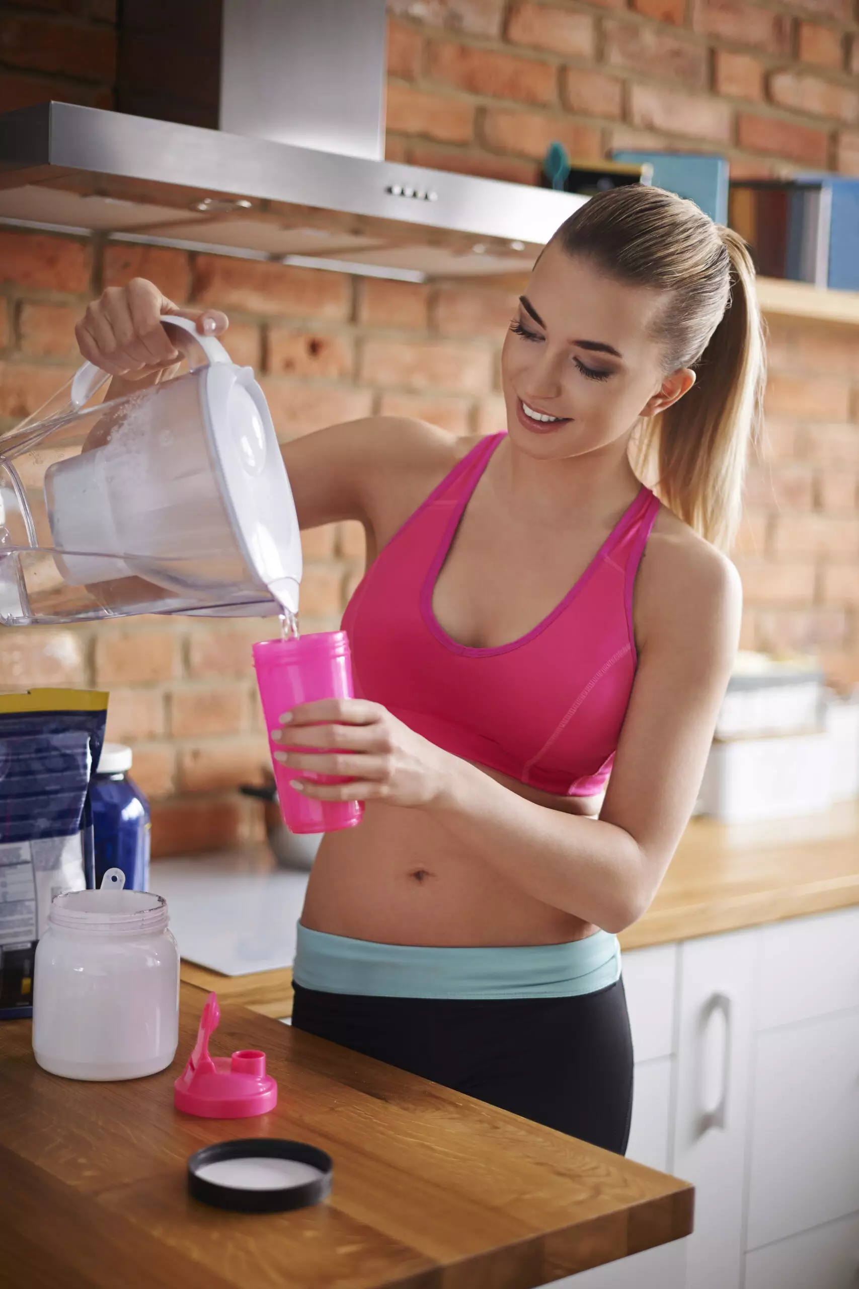Woman pouring water in kitchen for workout hydration.